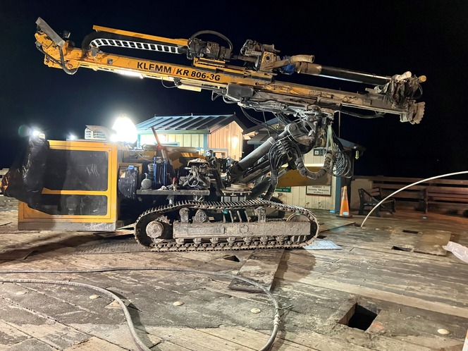 Construction drilling machine on a wooden platform at night with a background building and bright lighting