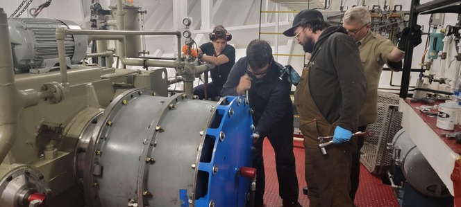 Four people working on a large industrial machine with tools inside a ferry's engine room
