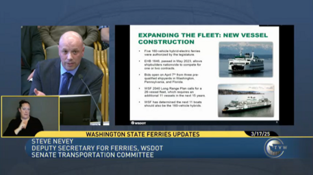 Screenshot of a TVW recording of a meeting showing a person speaking at a microphone beside a presentation slide on ferry fleet updates