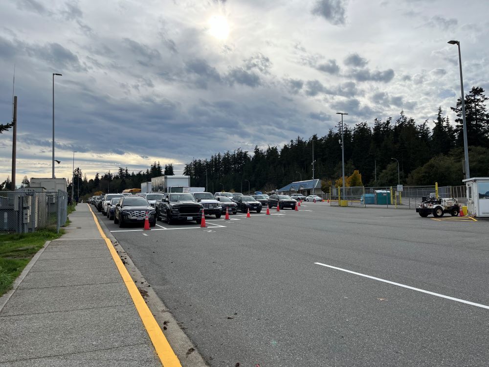 Anacortes terminal vehicle holding lanes with cars, traffic cones and a background of trees under a cloudy sky
