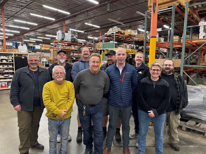 A group of ten people smiling inside a warehouse with shelves and boxes in the background