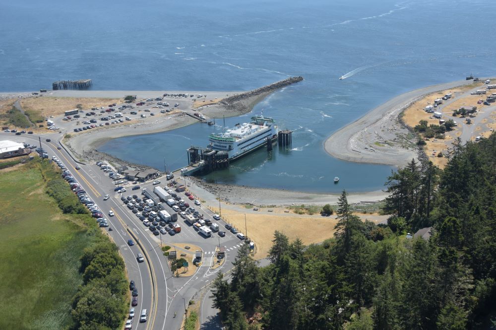 Aerial view of a ferry terminal with a ferry docked, surrounded by roads, parking areas and coastline