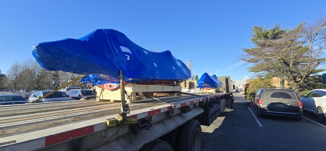 Flatbed trailer with blue tarp covering rescue boats in a parking lot
