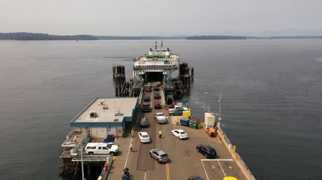 Vehicles boarding a ferry at Fauntleroy terminal with another ferry seen off Vashon Island in the background under a hazy sky