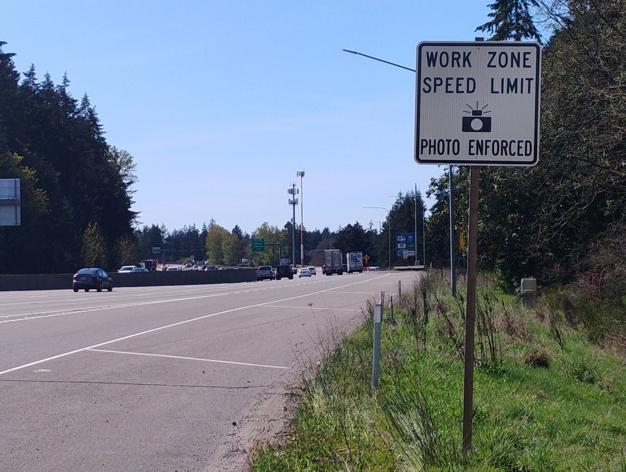 Highway scene with a "WORK ZONE SPEED LIMIT PHOTO ENFORCED" sign by the roadside