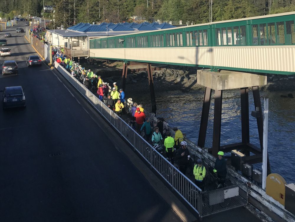 People with bicycles walking along a pathway along a road at Anacortes terminal below the overhead passenger loading