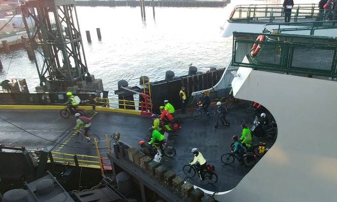 Cyclists, many in bright jackets pedaling off a ferry onto a dock