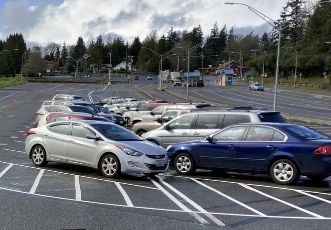 Cars parked in a lot at Southworth terminal with striped lines, trees, and a cloudy sky in the background
