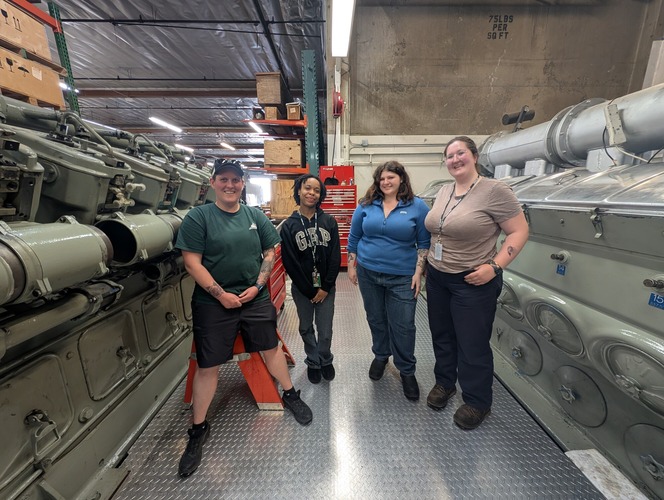 Four people standing between industrial machines in a workshop.