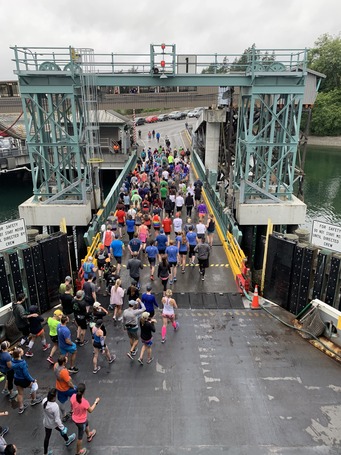 A large group of people in colorful athletic clothing walk off a ferry and onto a dock during an event.