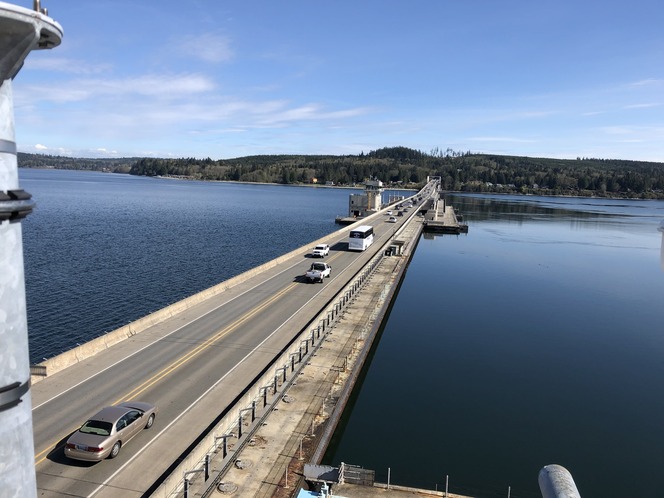 Bridge over a calm body of water with vehicles traveling under a clear blue sky.