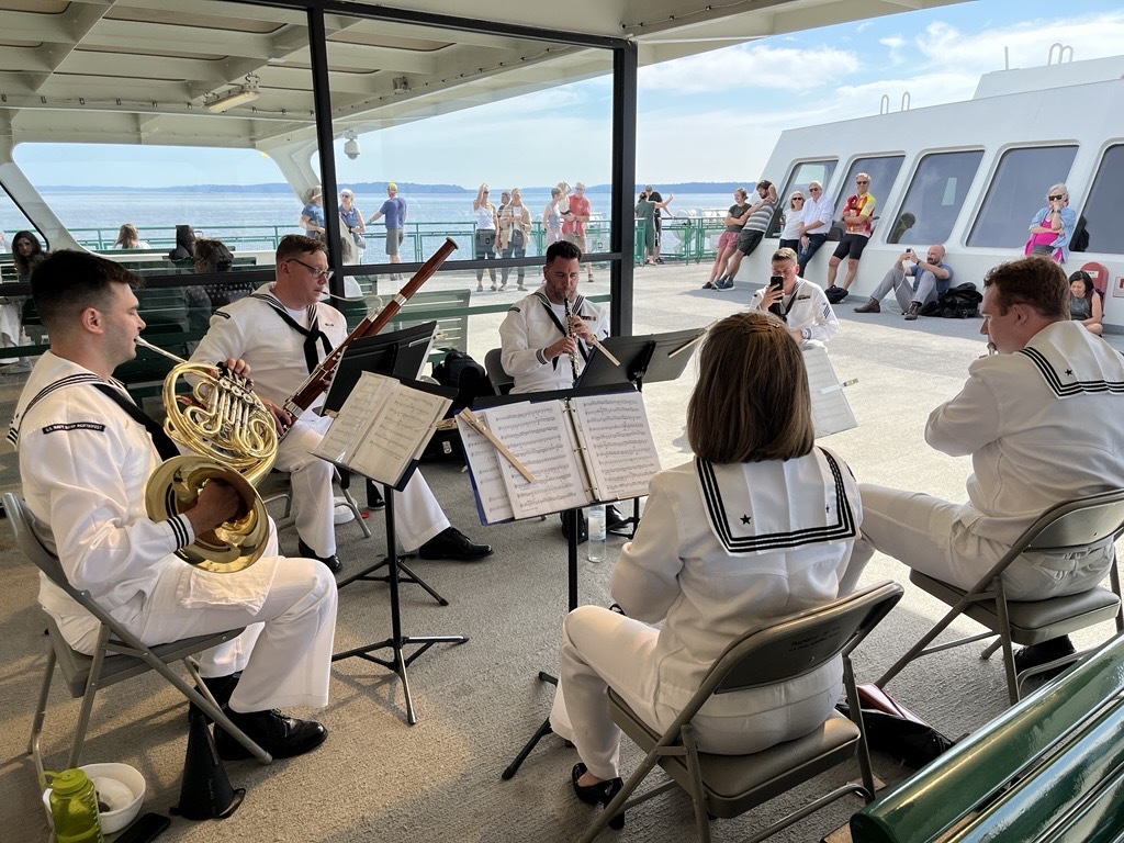 A quintet in white uniforms performing on a ferry deck with spectators watching.
