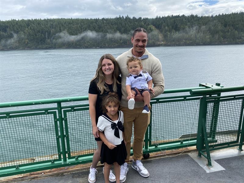 A family of four on a ferry with water and trees in the background.
