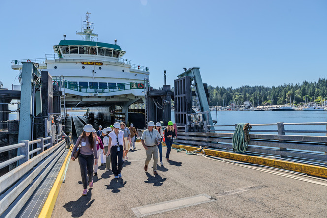 People in hard hats walking down a ferry ramp from the ferry "WENATCHEE" on a sunny day.