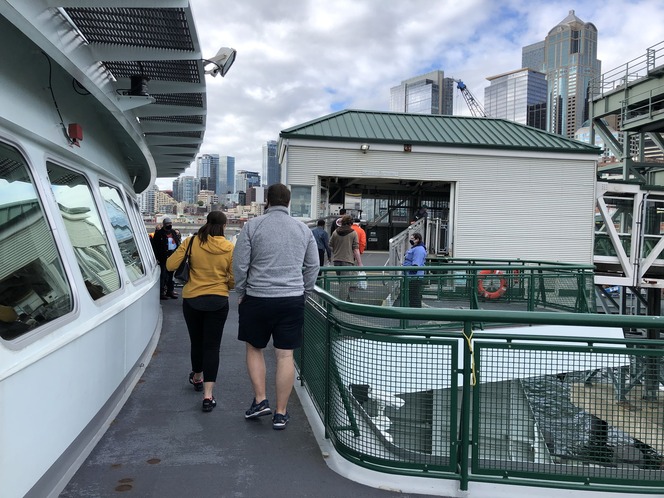 Passengers walking on a ferry gangway with skyscrapers in the background.