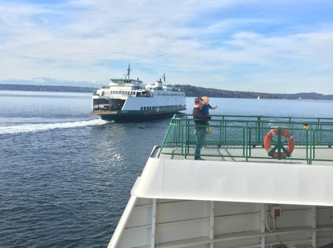 Two ferries on water, one with a person holding a child on deck.