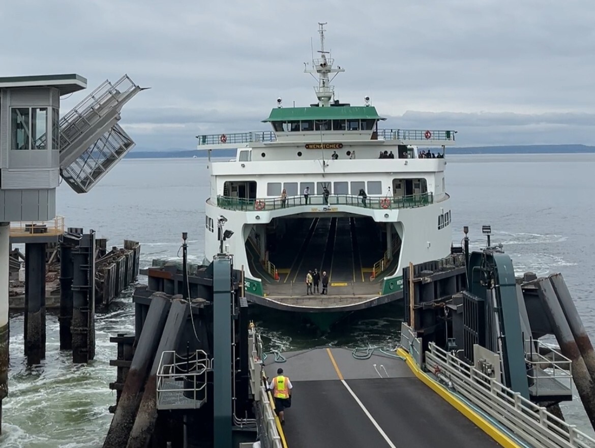 A ferry named "Wenatchee" approaching a dock at a terminal with a cloudy sky in the background.