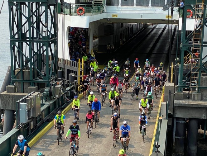 Cyclists riding off a ferry ramp onto a dock. 