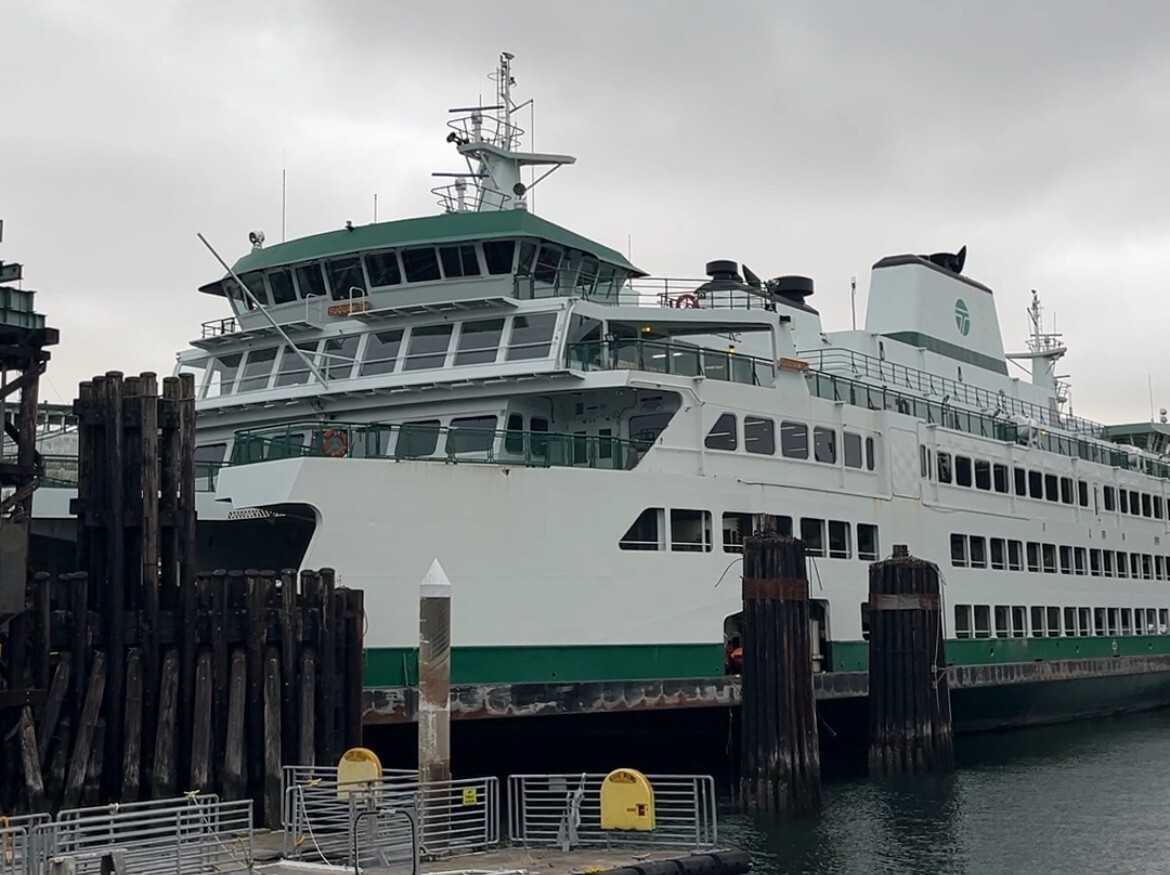 A large white and green ferry docked at a wooden pier under grey, cloudy skies.