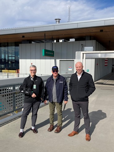 Three people standing on an outdoor walkway in front of Seattle terminal building.