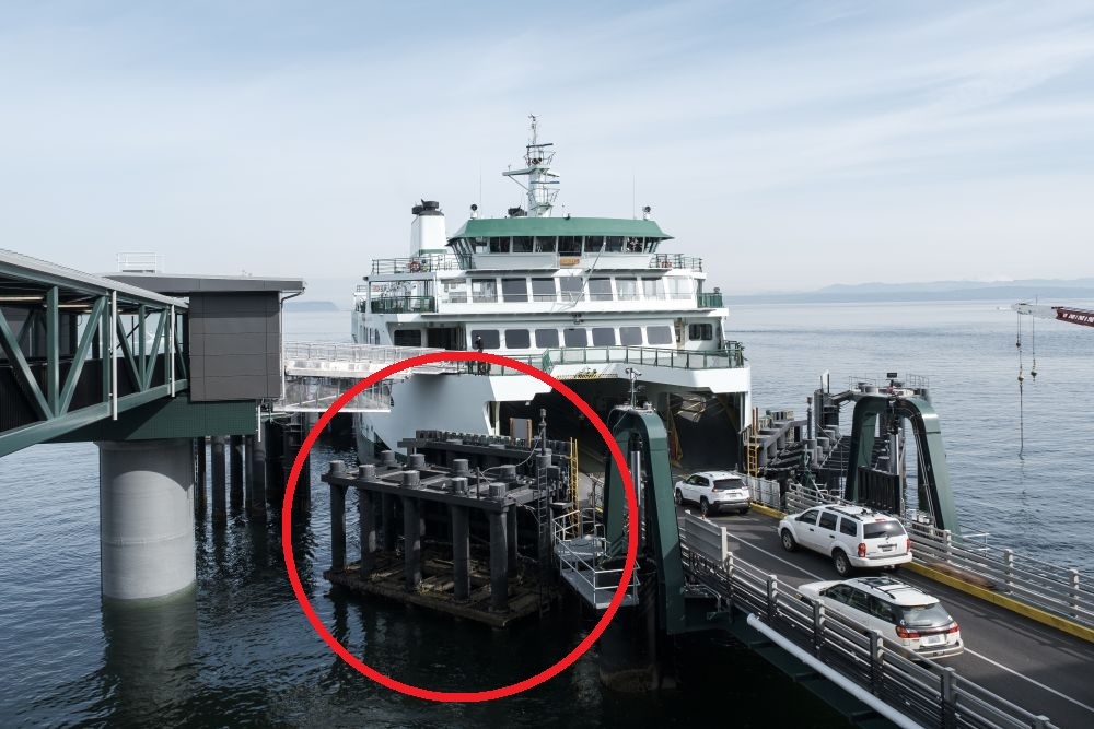 A ferry docked at a terminal with vehicles disembarking and a red circle around an in-water structure.