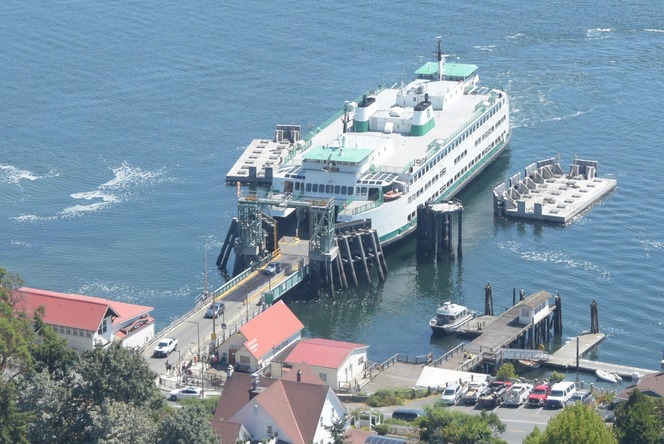 Aerial view of a ferry docked at Orcas Island terminal with red-roofed buildings and vehicles leaving the ferry.