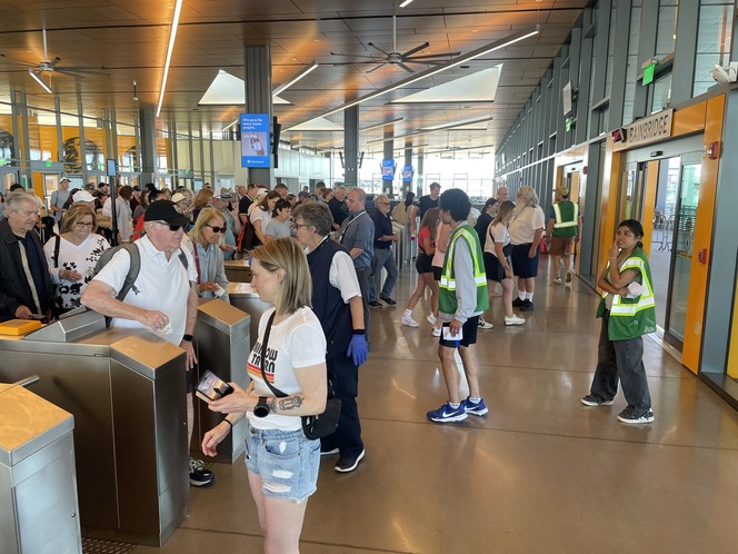 Inside Seattle terminal building with people passing through turnstiles and young adult volunteers in safety vests.