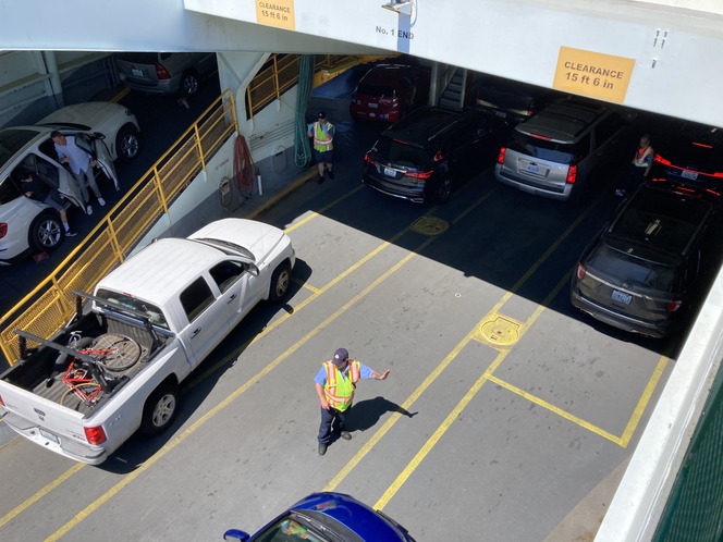 Traffic lanes on a ferry with various vehicles, a white pickup with a bicycle and a person in a safety vest.