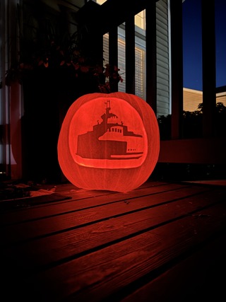A carved pumpkin with a ship design, glowing on a wooden porch at night.