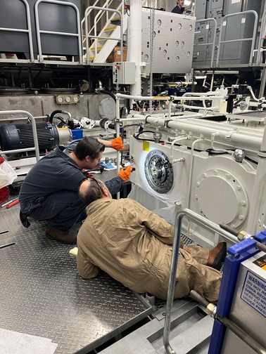 Two workers examine machinery in an industrial setting.