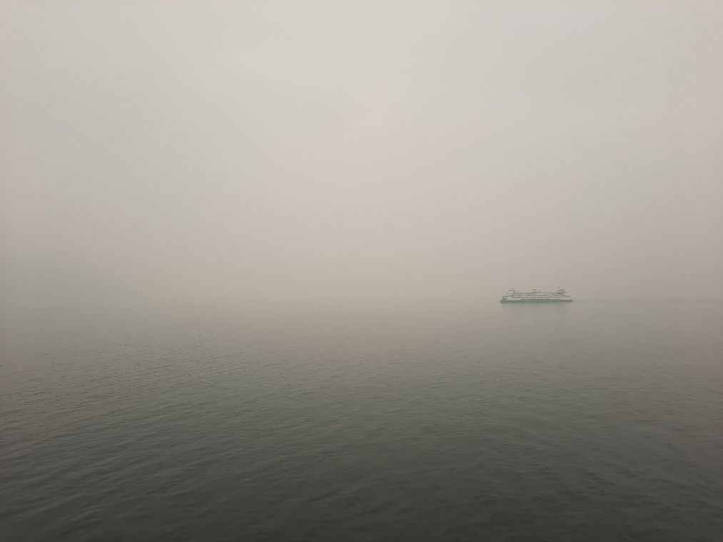 A ferry moves across a misty expanse of water with a foggy sky above.