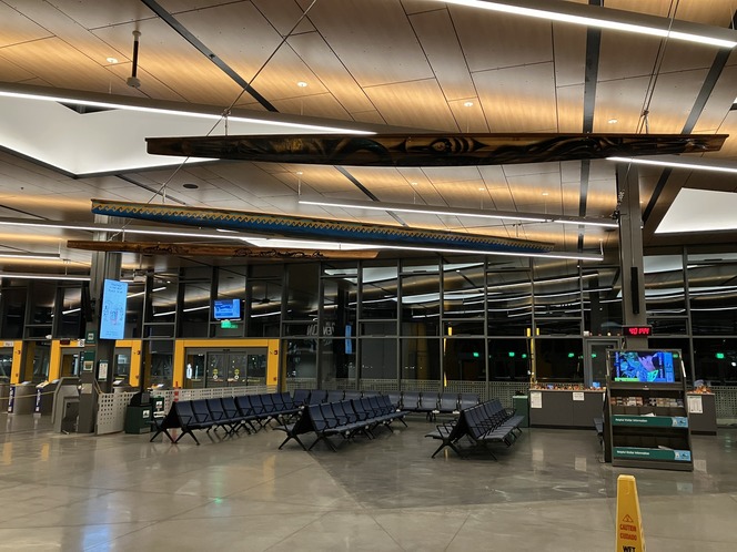 Spacious waiting area with blue seats, wooden ceiling panels and suspended canoes.