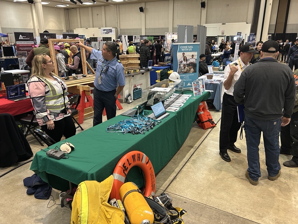 Indoor event with booths and attendees, featuring a table with safety gear and informational materials.