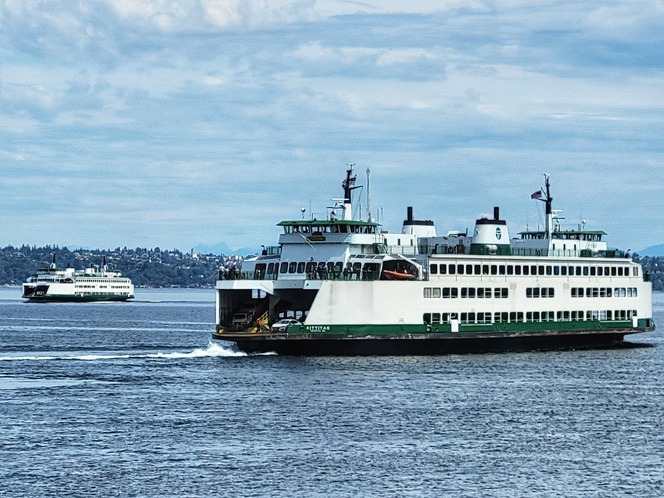 Two ferries on a body of water with a cloudy sky and distant shoreline.