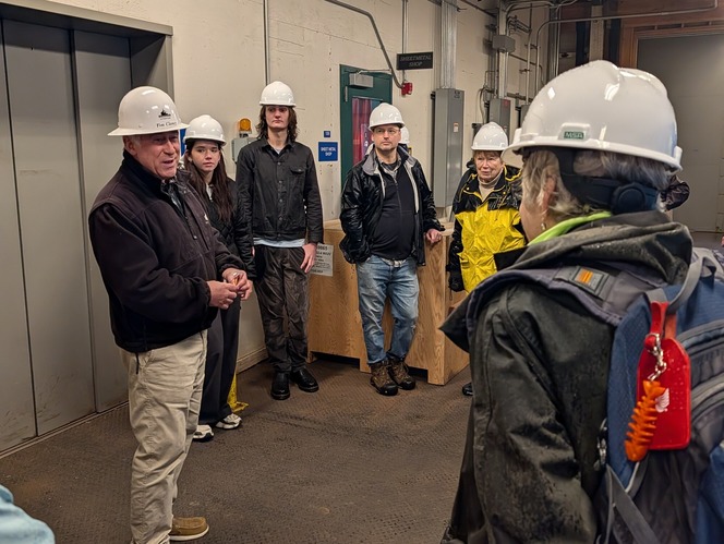 Group of people in hard hats gathered in an industrial room.