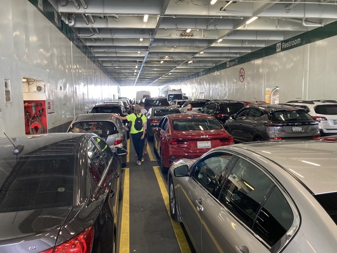 Crowded car deck on a ferry with parked vehicles and a person walking between them.