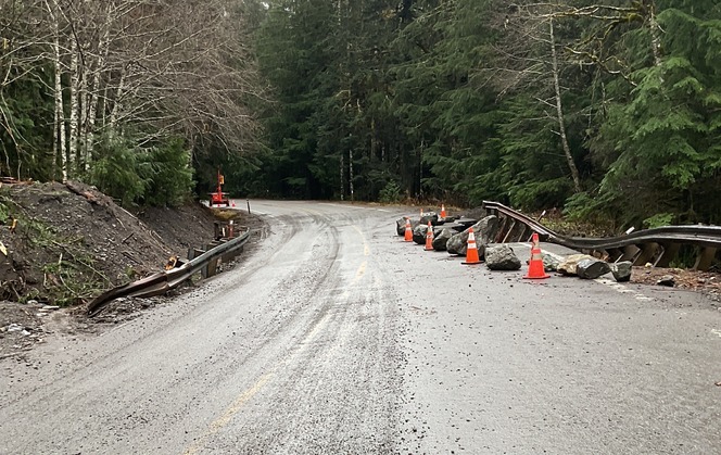 A rural portion of State Route 542 with damaged pavement and guardrail. rocks and orange cones protect a missing section of the pavement.