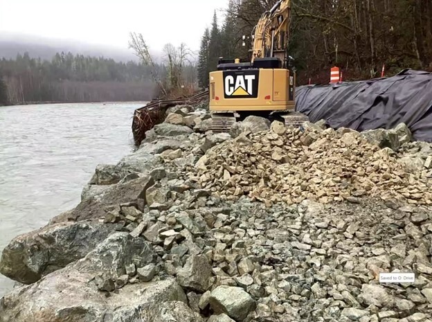 A yellow excavator sits atop rock that has been placed along the Sauk River to repair a roadbed for SR 530 that was washed away in December.