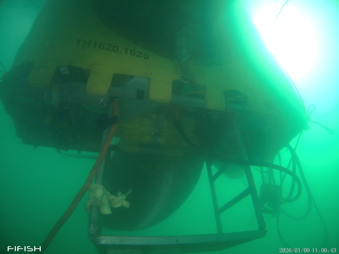 Underwater view of a yellow structure with cables and a mechanical arm.