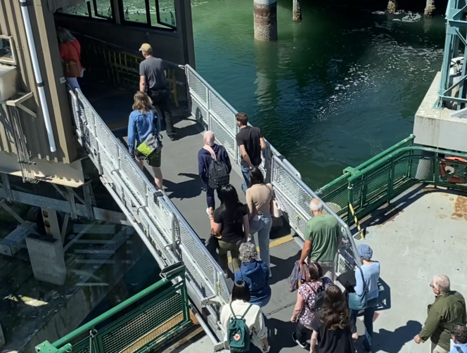 People walking up a metal gangway off a ferry to a terminal.
