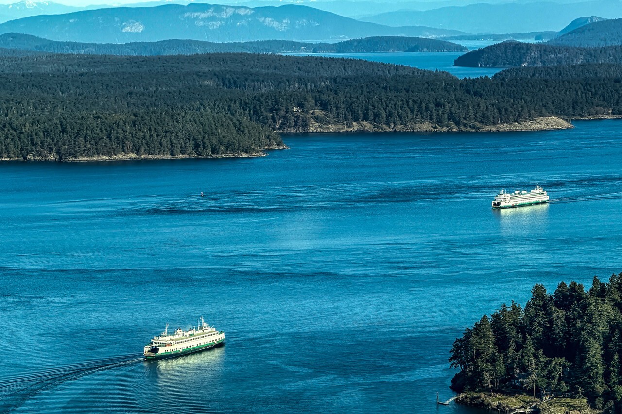 Aerial view of two ferries sailing on clear blue waters between forested islands.