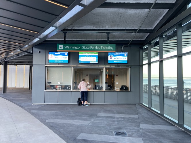 Ticket booths at Colman Dock in Seattle with digital screens and customer.