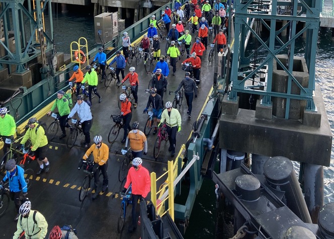 Cyclists in colorful attire walk their bikes onto a ferry.