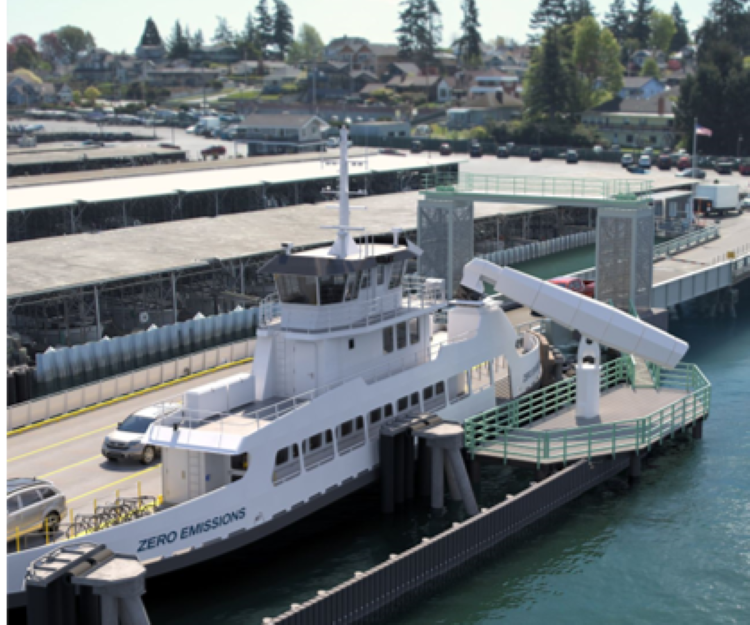 A white ferry labeled "ZERO EMISSIONS" docked at a terminal with a prominent arm-like structure going to the vessel.