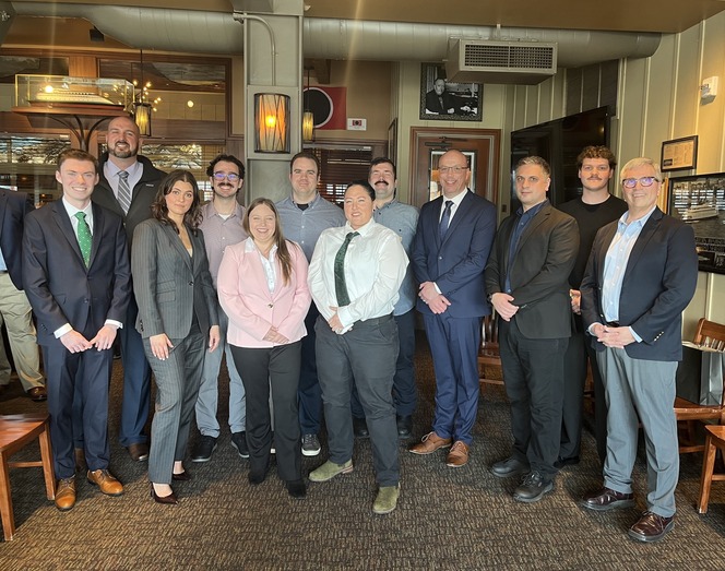 A group of 12 people in business attire pose in a warmly lit restaurant.