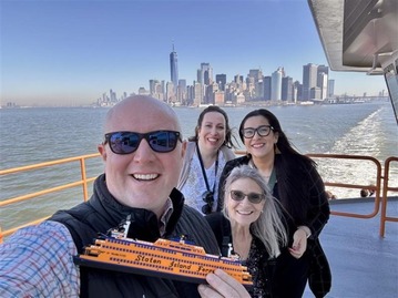 A group of four people on a ferry with the New York City skyline in the background.
