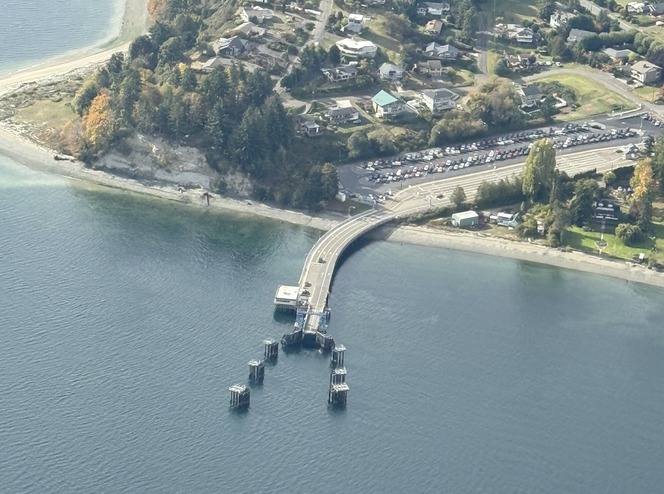 Aerial view of Southworth terminal with building at end of dock and parking, houses and trees in the background.