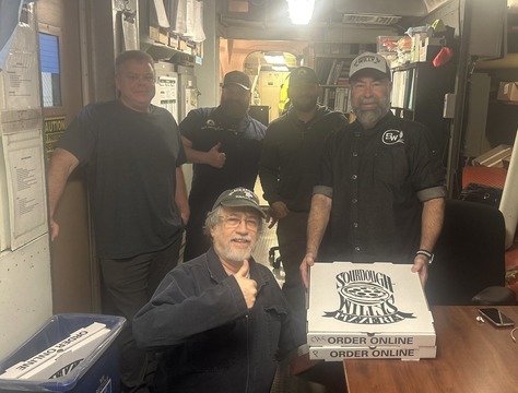 Five people in a ferry's engine room with one holding pizza boxes labeled "Sourdough Willy's Pizzeria."