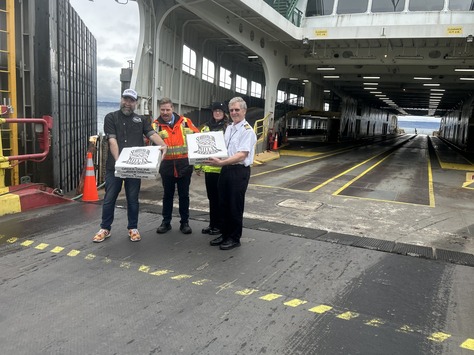 Four people holding boxes on a ferry deck with an open ramp.