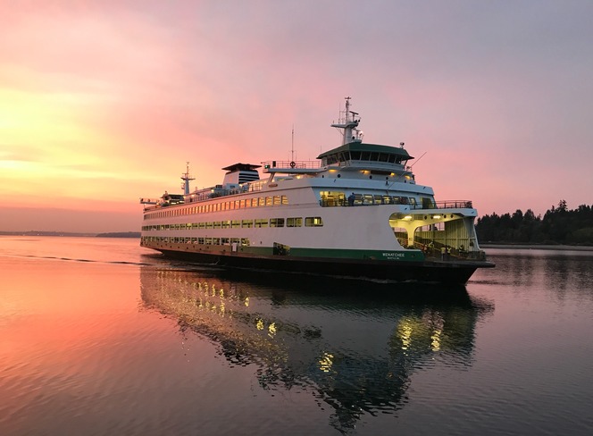 A ferry named "Wenatchee" on calm waters during a pink and orange sunset.